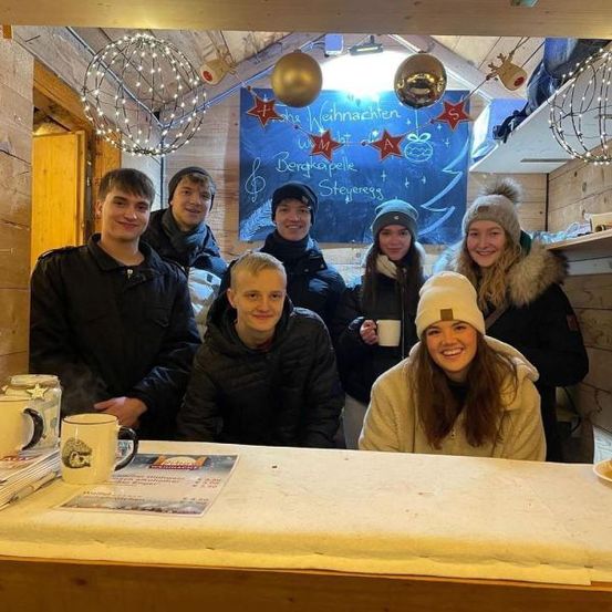 Eine Gruppe von Menschen lächelt und posiert für ein Foto in einem Raum mit einer Holzwand und Weihnachtsdekoration.