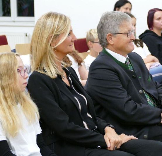 Mehrere Personen sitzen in einem Konferenzraum, wobei eine Frau und ein Mann sich anschauen und lächeln.