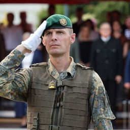 Ein Soldat salutiert vor einer Gruppe von Menschen, einige in Anzügen.