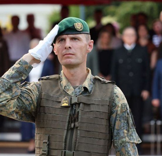 Ein Soldat salutiert vor einer Gruppe von Menschen, einige in Anzügen.