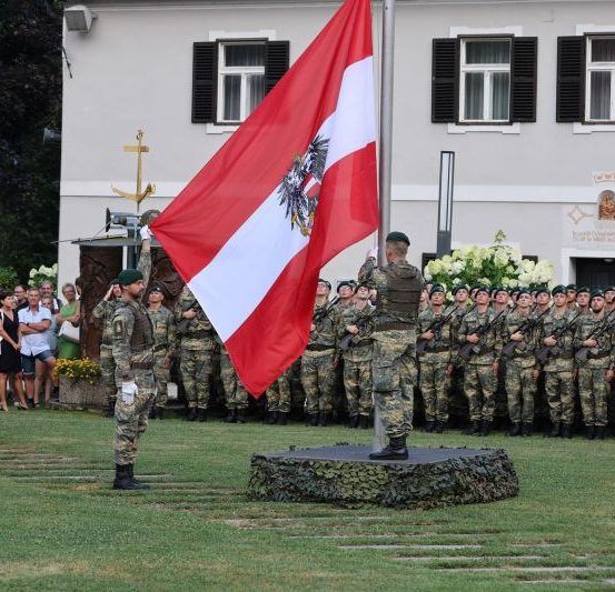 Soldaten hissen eine Flagge vor einem Gebäude mit Zuschauern.