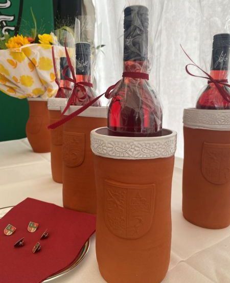 Fünf Tonflaschen mit Wein darin, in Plastik eingewickelt, und eine rote Serviette mit Nadeln auf einem Tisch.
