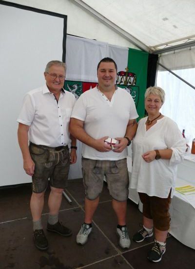 Drei Menschen stehen eng beieinander in einem Zelt. Zwei Männer und eine Frau in traditioneller Kleidung. Sie lächeln in die Kamera.