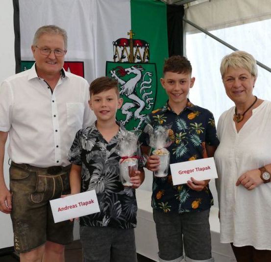 Zwei Jungen und zwei Erwachsene stehen vor einer weißen Wand. Sie lächeln und scheinen für ein Foto zu posieren. Sie halten ein Geschenk in den Händen.