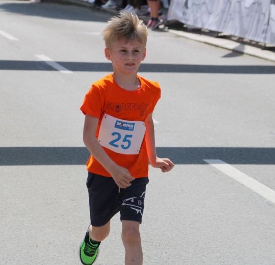 Ein Junge in einem orangefarbenen Shirt mit der Nummer 25 läuft einen Marathon.