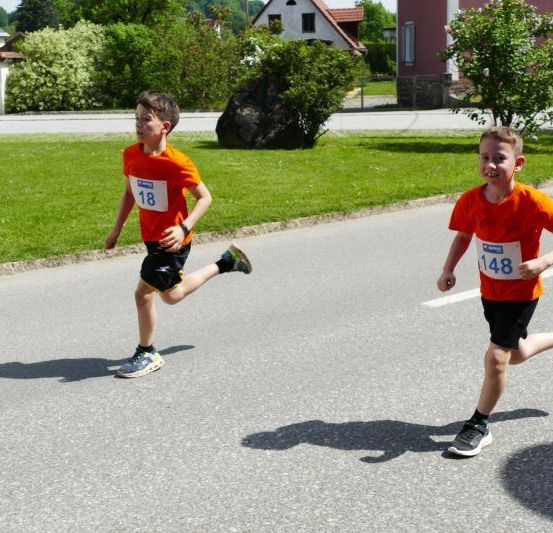 Zwei Jungen laufen in einem Rennen, einer mit der Nummer 18 und der andere mit 148 auf ihren Trikots.