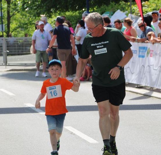 Ein älterer Mann mit einem grünen T-Shirt und ein Junge mit einem blauen Hut laufen einen Marathon, während Menschen hinter einer Barriere zusehen.