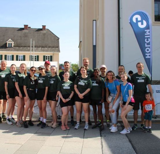 Eine Gruppe von Menschen in grünen und blauen Shirts posiert für ein Foto vor einem Gebäude.