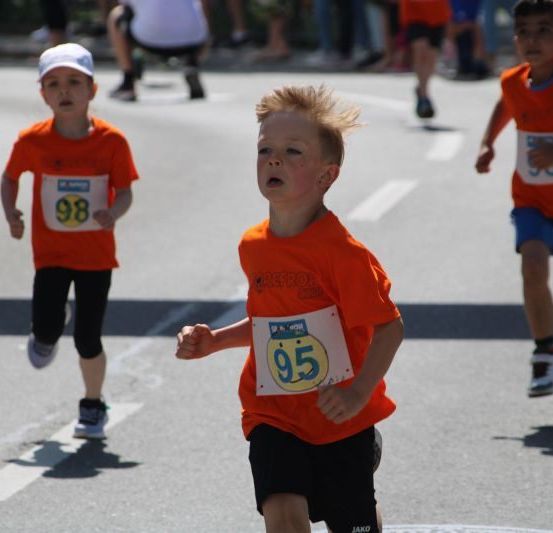 Drei Jungen in orangefarbenen Trikots mit Nummern laufen ein Rennen. Ein Junge ist Nummer 95.