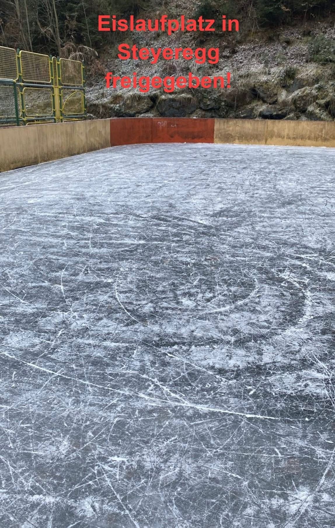 Eine leere Eisbahn mit einer Betonbarriere und einem roten Abschnitt, umgeben von einer felsigen Wand.