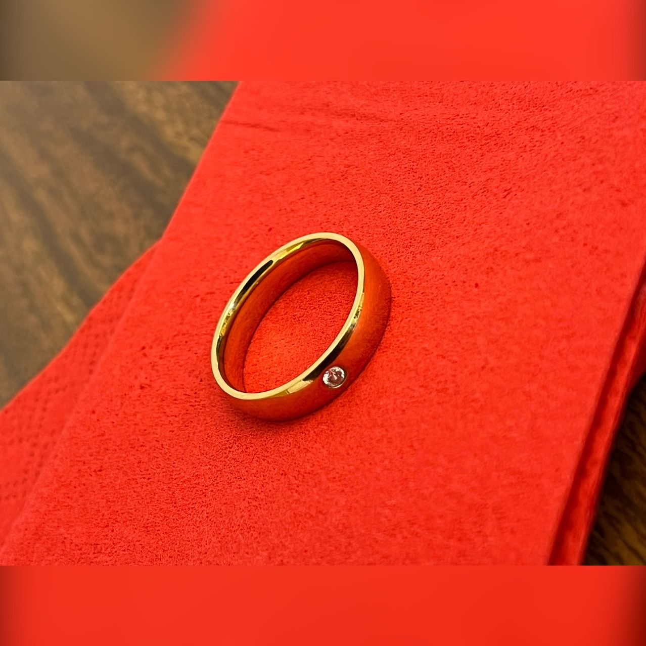 Ein Goldring mit einem Diamanten liegt auf einem roten Tuch. Der Ring hat eine polierte Oberfläche und ruht auf einer Holzoberfläche.