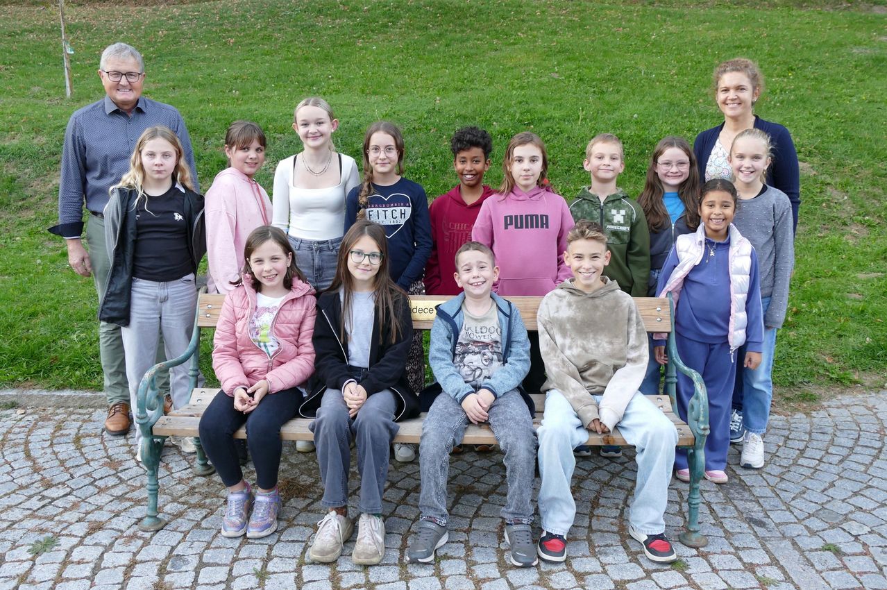 Eine Gruppe von Kindern und zwei Erwachsenen lächelt und posiert für ein Foto in einem Park, sitzt auf einer Bank und steht dahinter.