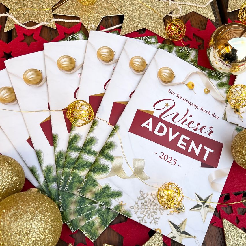 Eine Reihe festlicher Karten mit Weihnachtsthema. Die Karten sind gold und weiß, mit einem roten Rand. Die Karten tragen den Text 'Wieser Advent 2025'. Sie liegen auf einem roten Tuch mit goldenen und silbernen Ornamenten.