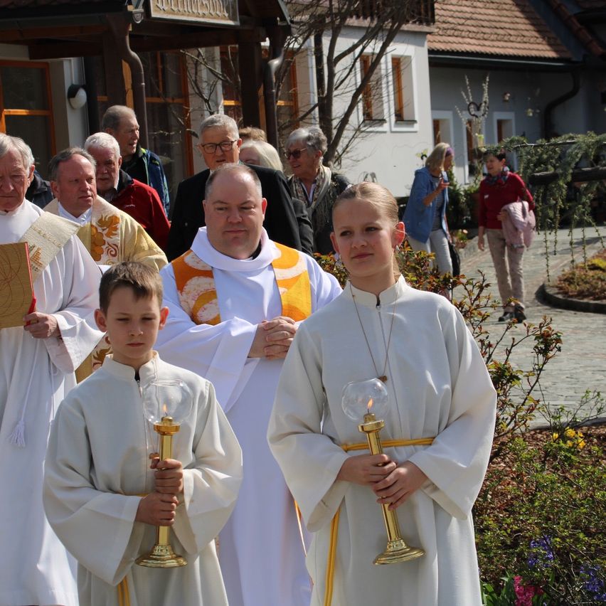 A group of priests and children in white robes hold lit candles outside a church during a procession.