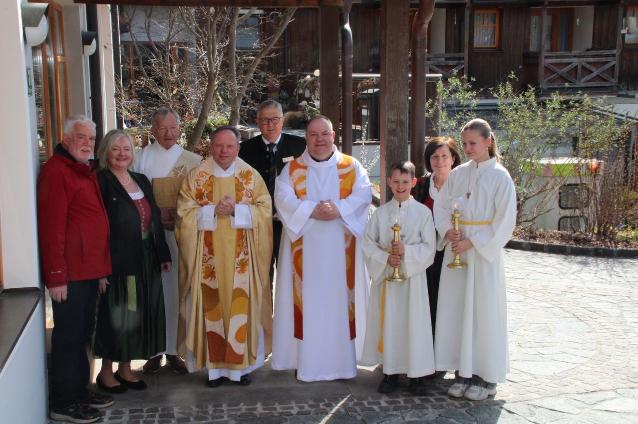 A group of people in clerical robes stand outside a building. They are holding candles and smiling. There is a man in a suit behind them.
