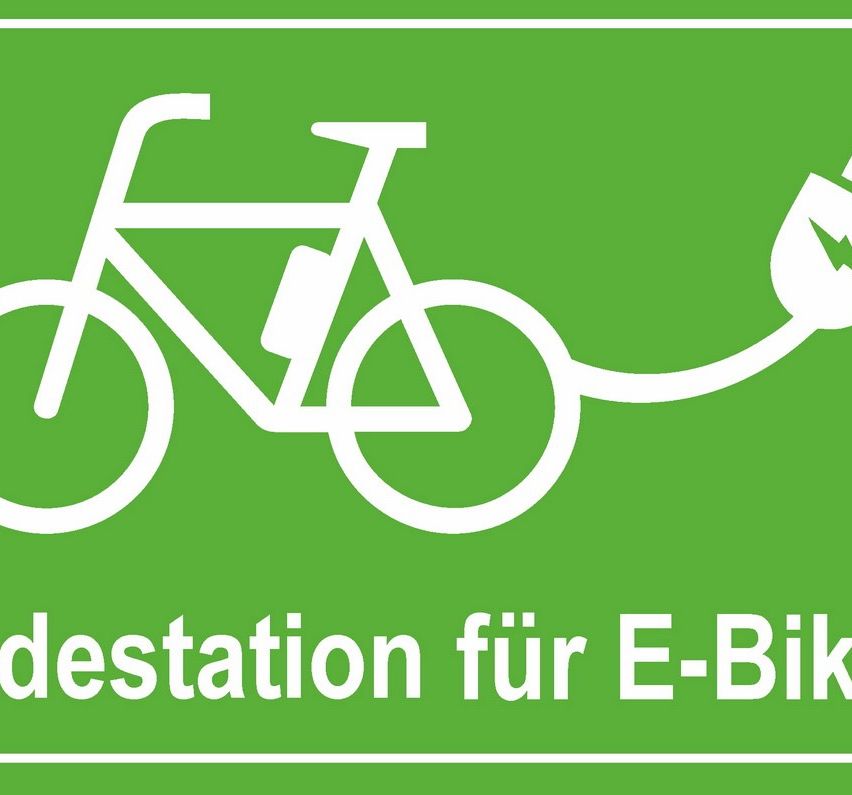 Grüner Schild mit weißem Fahrrad-Symbol und Text 'E-Bike-Ladestation'. Das Fahrrad hat eine Flasche am Rahmen befestigt.