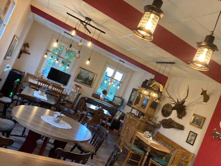 Ein gemütlicher Essbereich mit runden Tischen, Stühlen und einem Kamin. Es gibt hängende Lampen, Hirschköpfe und Bilderrahmen an der Wand.