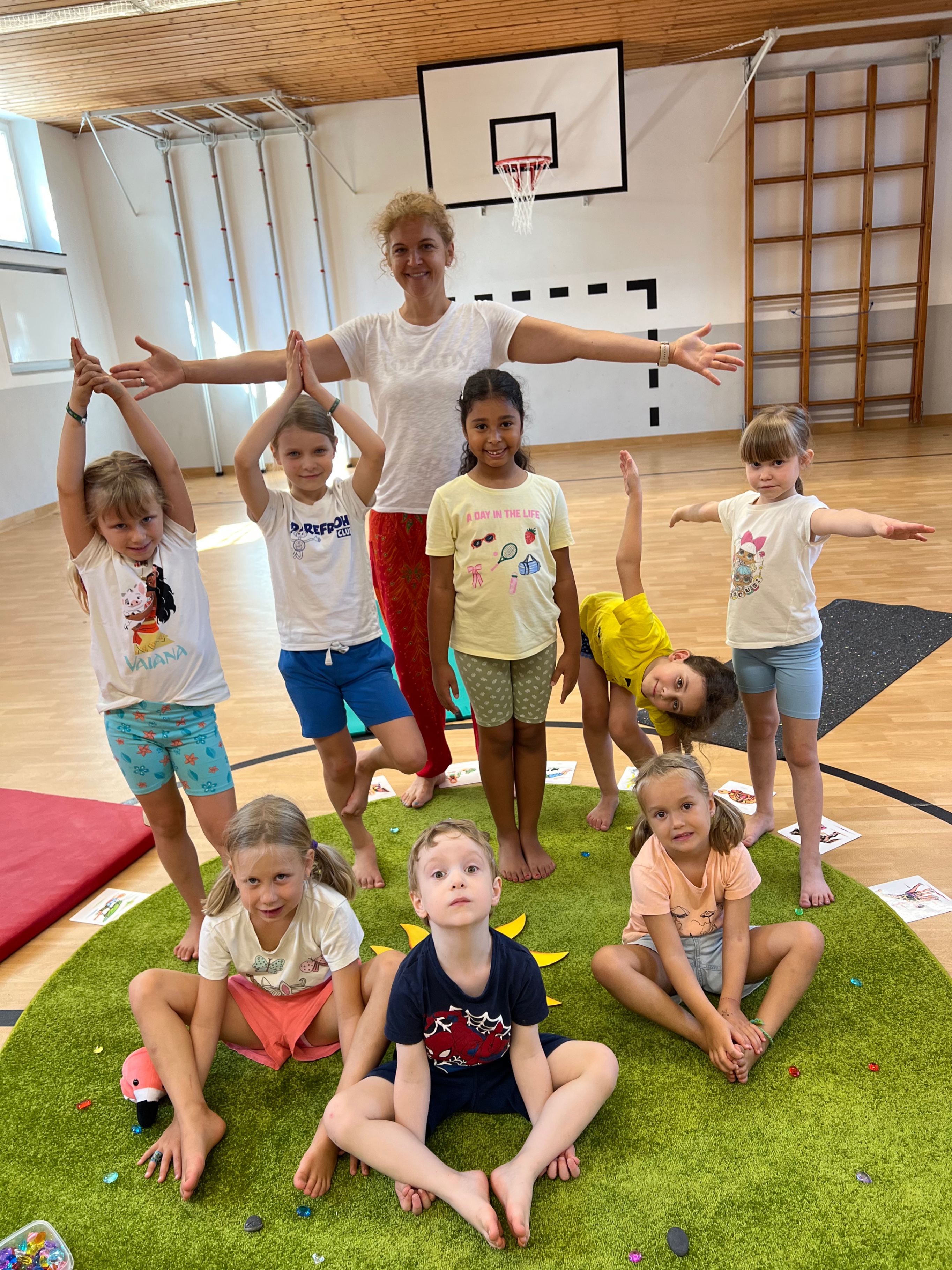 Kinder und Trainerin machen Yogaübungen in einer Sporthalle in Österreich.