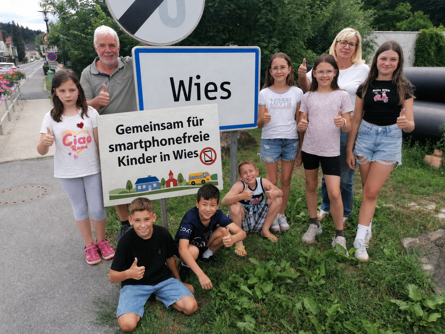 Wies: Kinder und Erwachsene mit Daumen hoch vor Schild für smartphonefreie Kinder