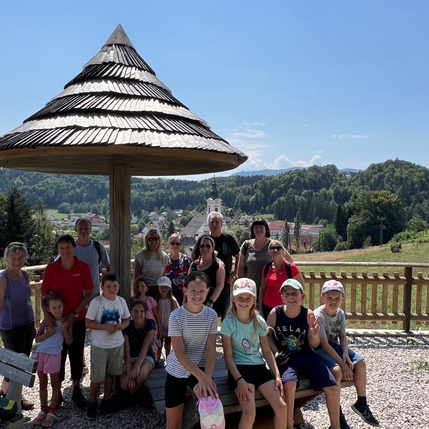 Eine Gruppe von Menschen, einschließlich Erwachsener und Kindern, posiert für ein Foto unter einem hölzernen Pavillon mit einem malerischen Bergblick im Hintergrund.