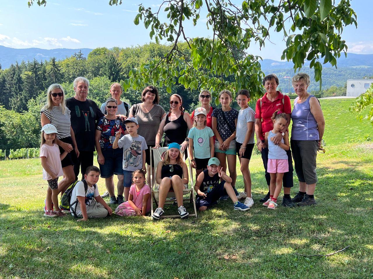 Eine große Familie mit Erwachsenen und Kindern posiert für ein Foto in einem Park unter einem Baum mit Bergen im Hintergrund.