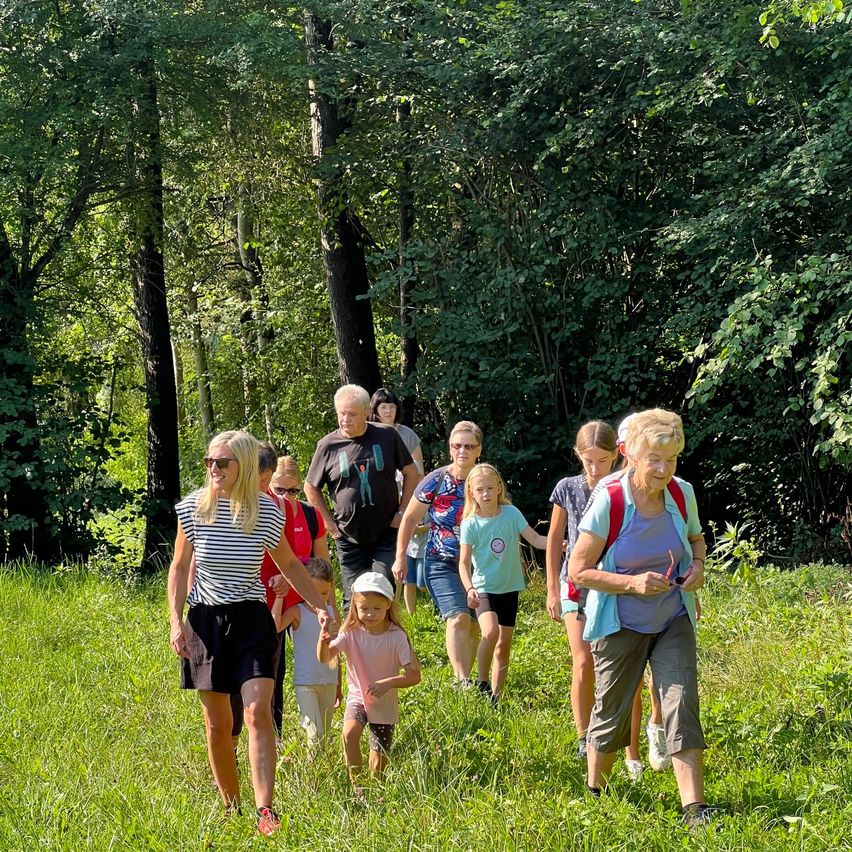 Eine Gruppe von Menschen, einschließlich Erwachsener und Kindern, wandert auf einem Grasfeld mit Bäumen im Hintergrund.