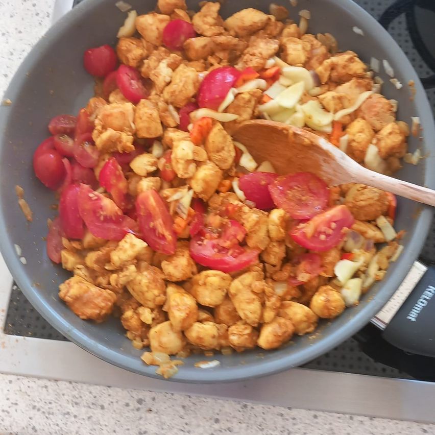 Eine Pfanne mit gekochtem Huhn, Tomaten und Gemüse auf einem Herd.