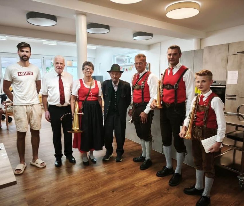 Eine Gruppe von Menschen in traditioneller deutscher Kleidung, die Musikinstrumente halten, steht in einem Raum.