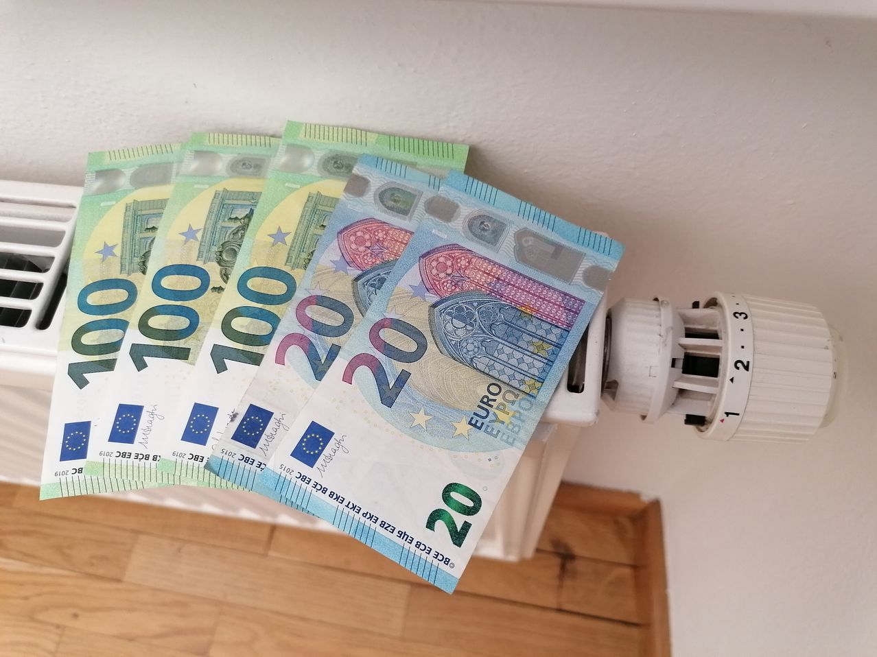 Ein Stapel von Euro-Banknoten mit einem Gesamtwert von 220 Euro, auf einem weißen Heizkörper mit Thermostat.