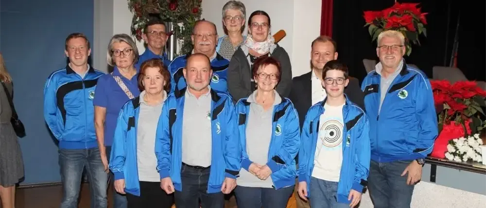 Eine Gruppe von Personen, die blaue Jacken tragen, einschließlich Männer und Frauen, posiert für ein Foto vor einem Hintergrund roter Blumen.