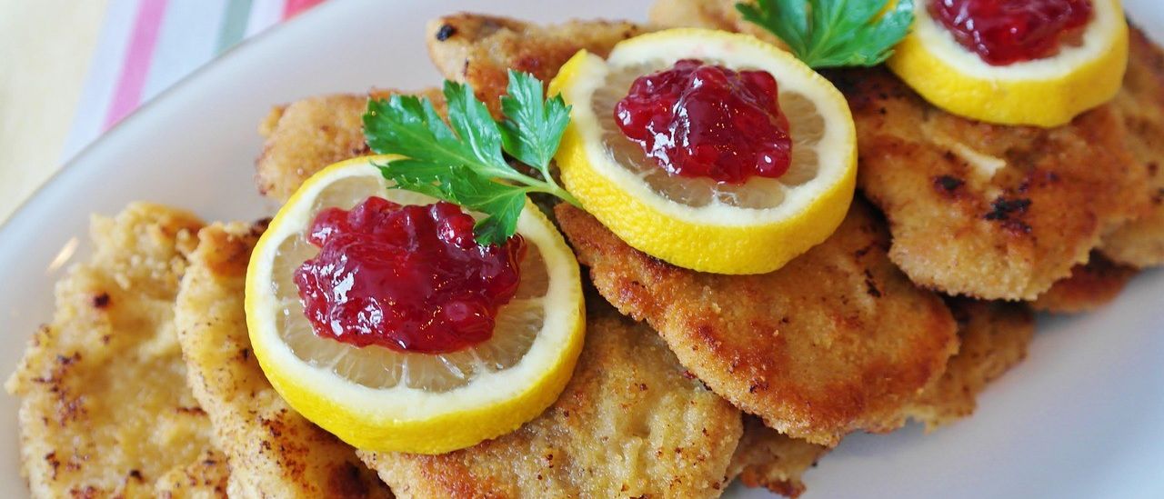 Ein Teller mit panierten Hähnchenschnitzeln mit Zitronenscheiben und roter Marmelade. Garniert mit Petersilienblättern.