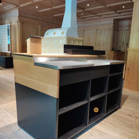 Eine moderne, schlanke Kücheninsel aus Holz und Metall mit weißer Arbeitsplatte und Regalen, in einem holzgetäfelten Raum mit Holzdecke und -boden.