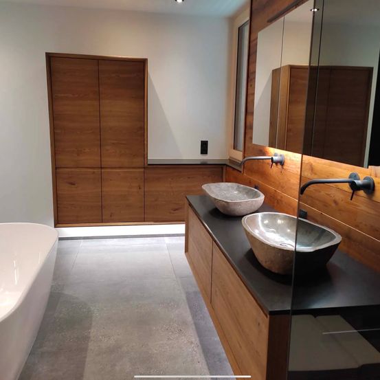 Modernes Badezimmer mit weißer Badewanne und Holzschränken. Zwei Waschbecken stehen auf einer schwarzen Theke.