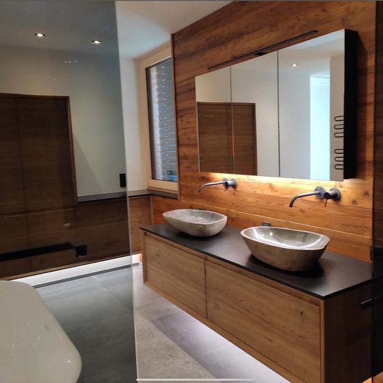 Ein elegant gestaltetes Badezimmer mit Holzwänden, zwei Waschbecken, einem Spiegel mit Lichtleiste und einer großen Badewanne.