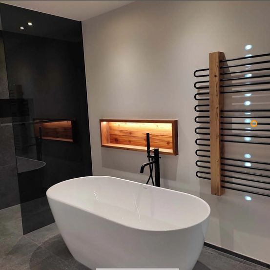Ein modernes Badezimmer mit einer weißen Badewanne, schwarzem Wasserhahn, hölzerner Ablage und einem wandmontierten schwarzen Spiralhandtuchhalter.