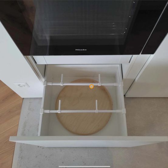 Eine Küchenschublade mit einem Holzbrett ist offen, und ein Miele-Ofen ist darüber platziert.