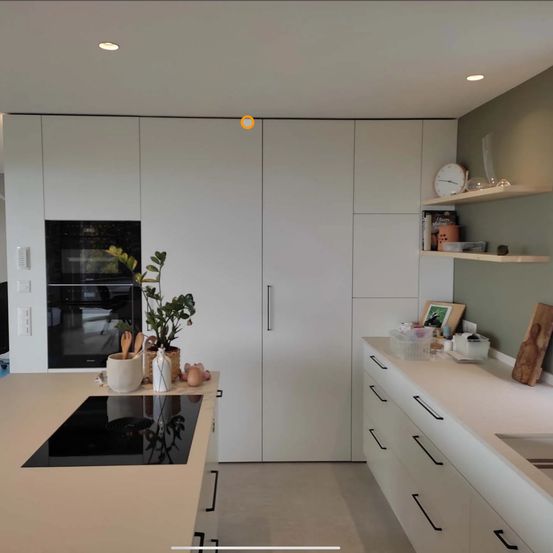 Eine moderne Küche mit weißen Schränken, einem Gasherd und einem Waschbecken. Es gibt Regale mit dekorativen Gegenständen und eine an der Wand montierte Uhr.