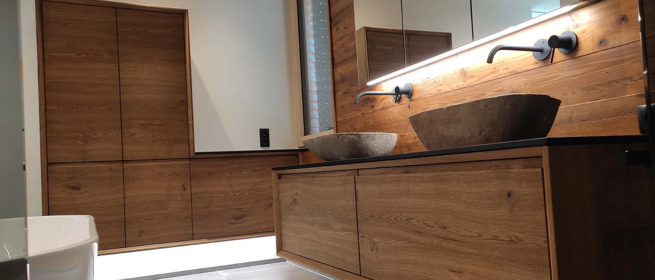 Innenansicht eines modernen Badezimmers mit zwei Waschbecken, Holzschrank und Holzwand. Die Wand hat einen Spiegel und einen Lichtstreifen.