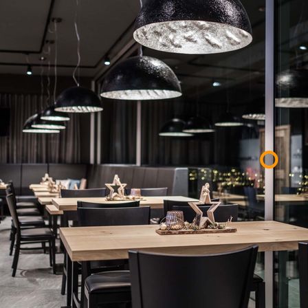 Ein modernes Restaurant-Interieur mit Holztischen, schwarzen Stühlen und großen schwarzen Lampen, die von der Decke hängen. Die Tische sind mit Holzsternen und anderen Ornamenten dekoriert.