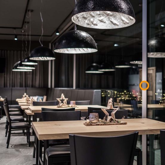 Ein modernes Restaurant-Interieur mit Holztischen, schwarzen Stühlen und großen schwarzen Lampen, die von der Decke hängen. Die Tische sind mit Holzsternen und anderen Ornamenten dekoriert.