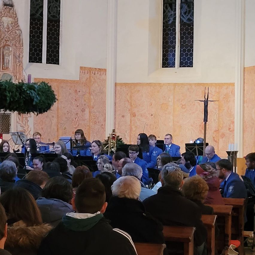 Ein Gottesdienst mit einem Chor, der vor einer großen Gemeinde aufführt, mit dekorativen Elementen und einem Kreuz an der Wand.