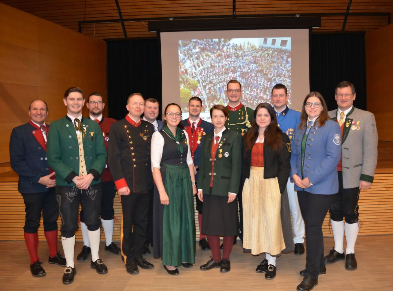 A group of people dressed in traditional uniforms pose for a photo in front of a large projection on a wall.