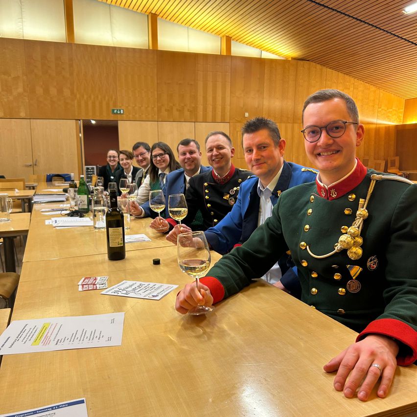 A group of people dressed in uniforms and holding wine glasses, sitting at a table in a conference room.