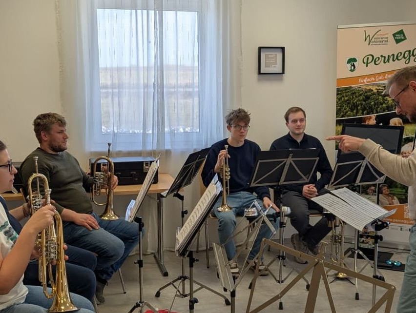 Eine Gruppe von Musikern übt in einem Raum mit Notenständern, eine Person zeigt.