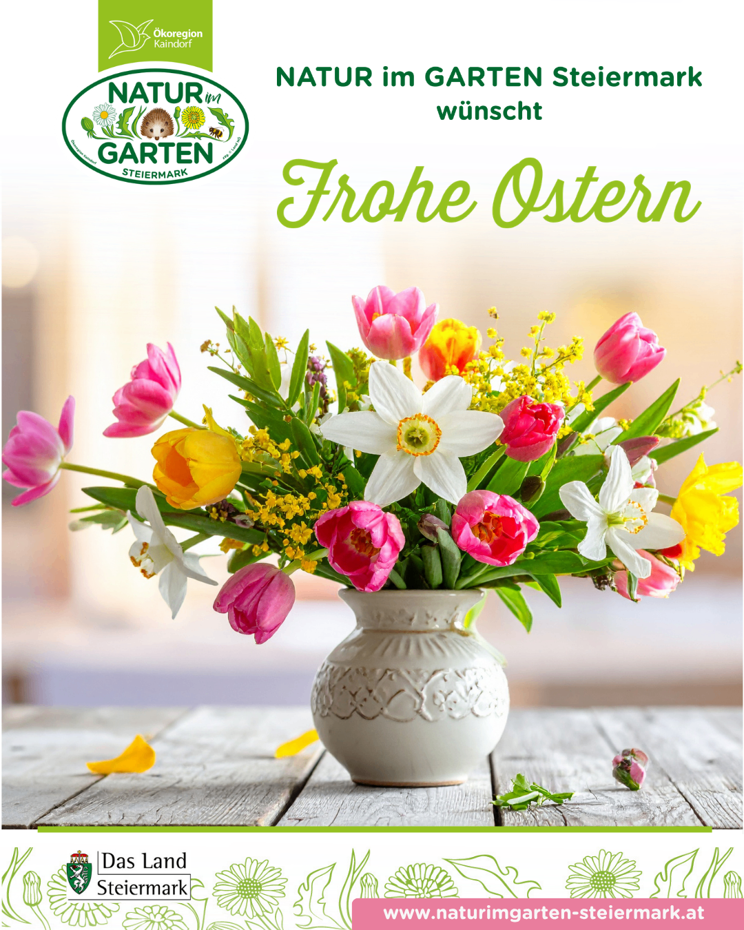 Eine weiße Keramikvase mit verschiedenen Blumen, darunter Tulpen und Narzissen, steht auf einem Holztisch. Das Bild ist wahrscheinlich ein Werbematerial für eine Gartenmarke, mit einem Wasserzeichen in der oberen linken Ecke.