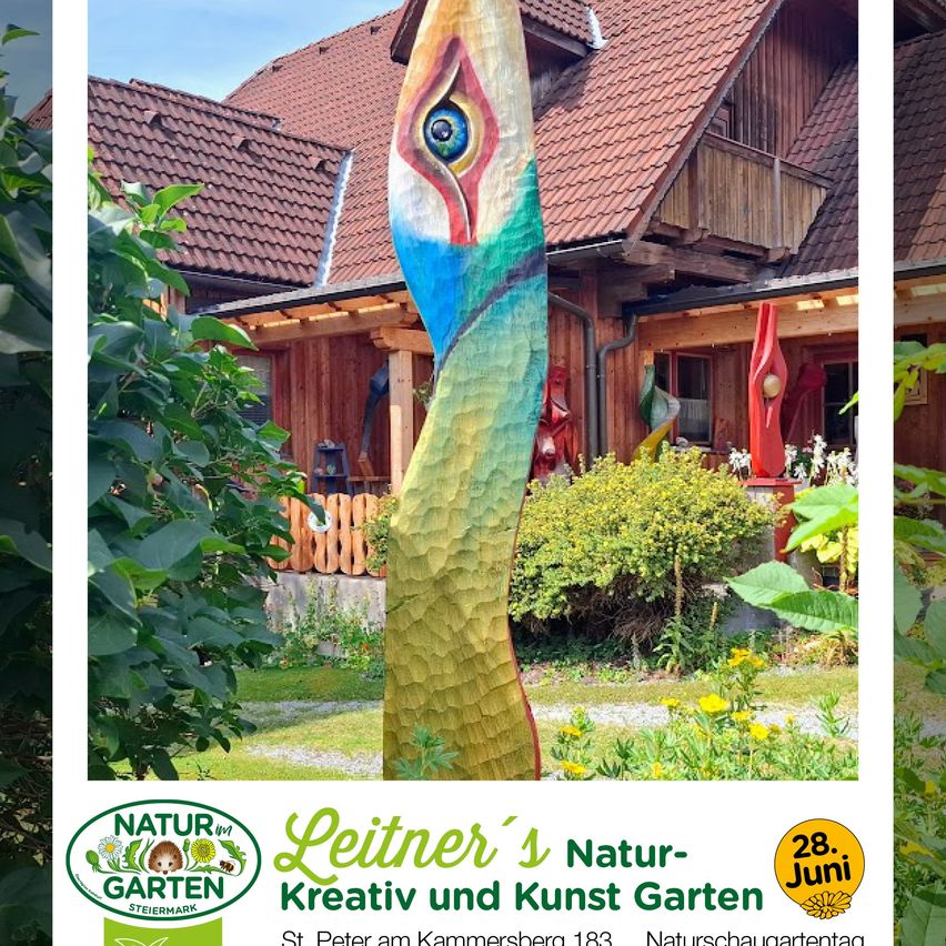 A colorful bird sculpture stands before a traditional wooden house with a red roof, surrounded by lush greenery and flowers. A poster below advertises the Leitner's Nature and Art Garden.