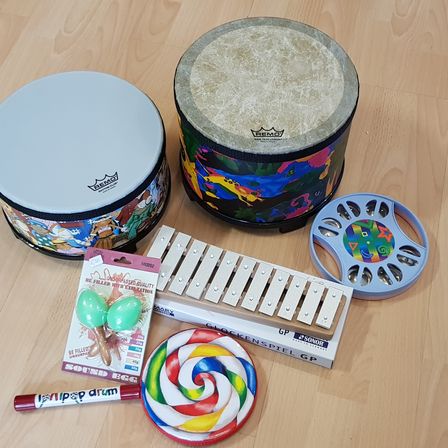 Ein Drum-Set mit zwei Trommeln, Maracas, einem Xylophon, einem Lollipop und einem Marker auf einer Holzoberfläche.
