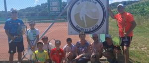 Eine Gruppe von Kindern und Erwachsenen posiert für ein Foto vor einem Tennisplatz mit einem Schild, das 'SU Tennisclub Murfeld Süd' steht.
