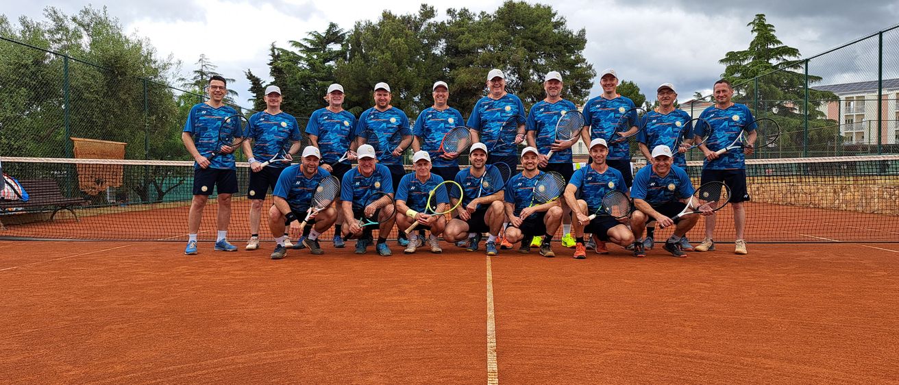 Eine Gruppe von Tennisspielern, in Blau gekleidet, posiert für ein Foto auf einem Tennisplatz unter einem bewölkten Himmel.