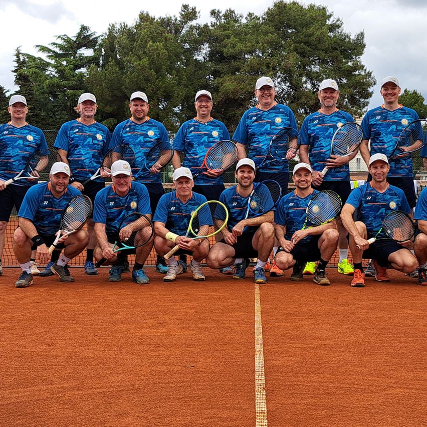 Eine Gruppe von Tennisspielern, in Blau gekleidet, posiert für ein Foto auf einem Tennisplatz unter einem bewölkten Himmel.